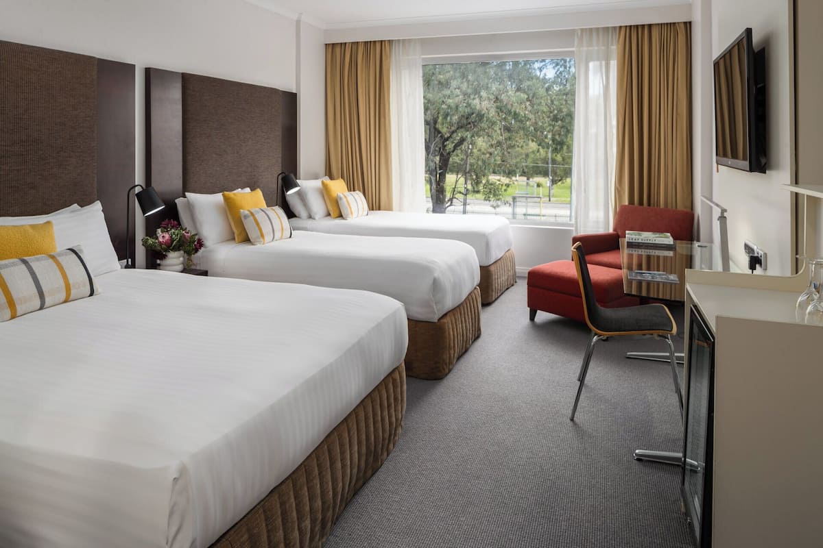 Ett hotellrum med två sängar, ett skrivbord, en stol och ett stort fönster med gardiner.