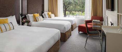 A hotel room with two beds, a desk, a chair, and a large window with curtains.