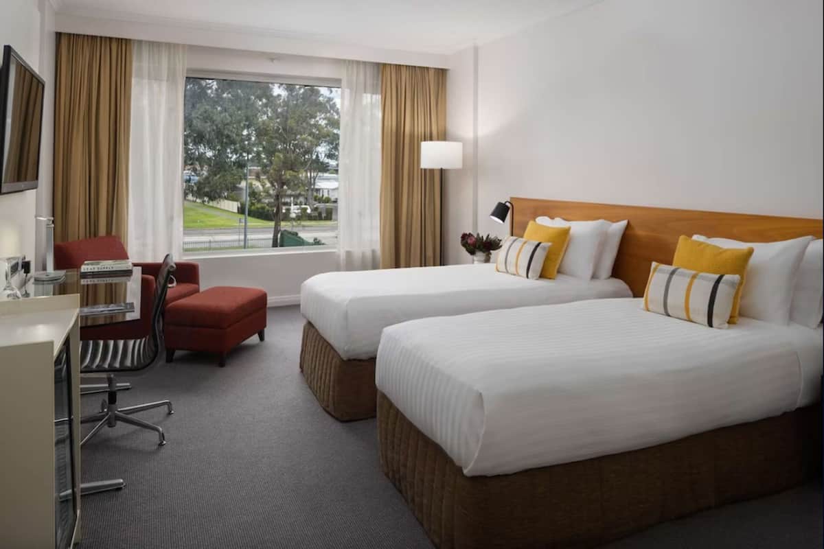 Ett hotellrum med två sängar, ett skrivbord, en stol och en TV.