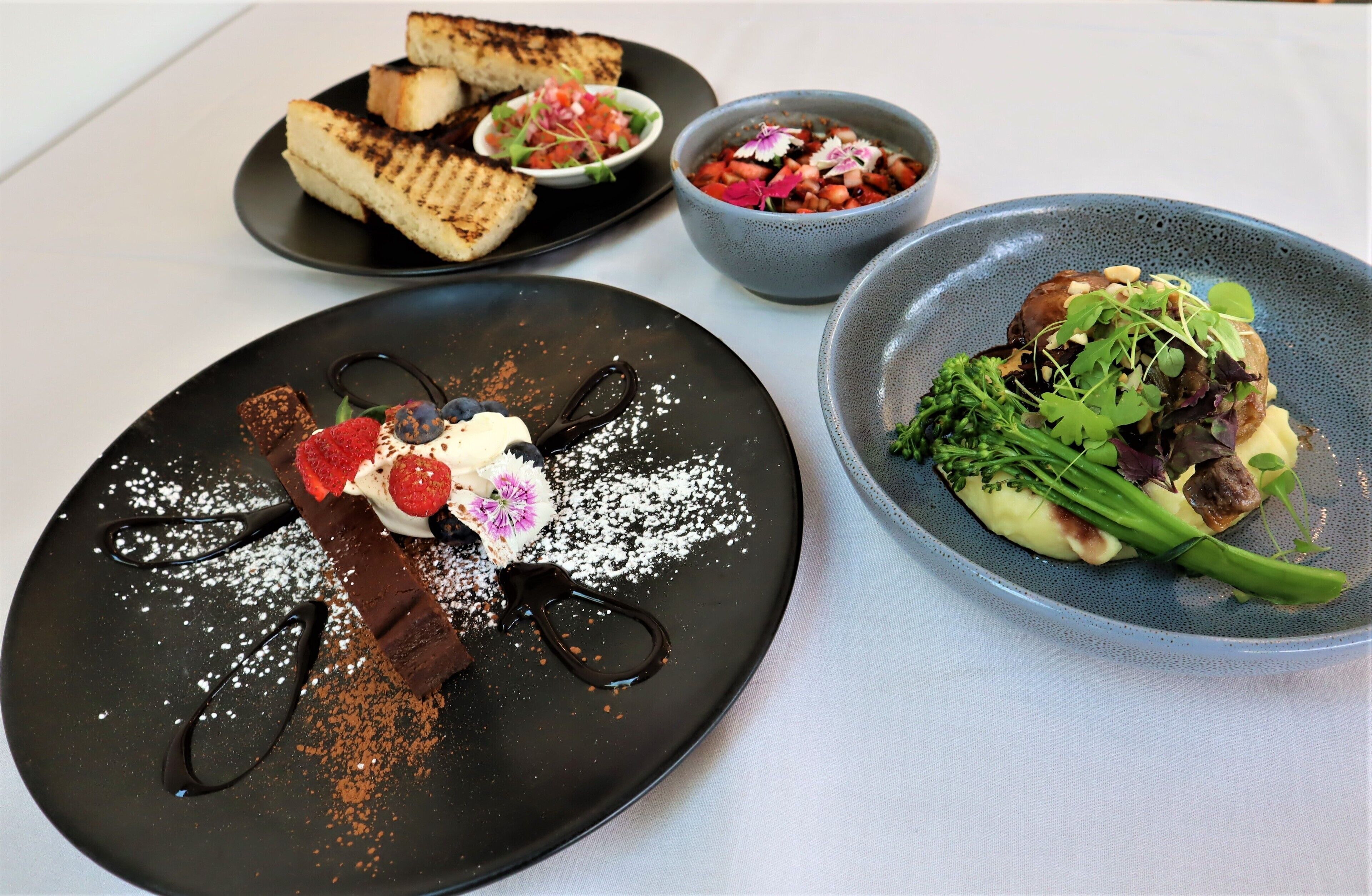 A variety of dishes on plates, including a dessert with chocolate and strawberries, a salad with greens and mushrooms, and a bowl of mixed vegetables.