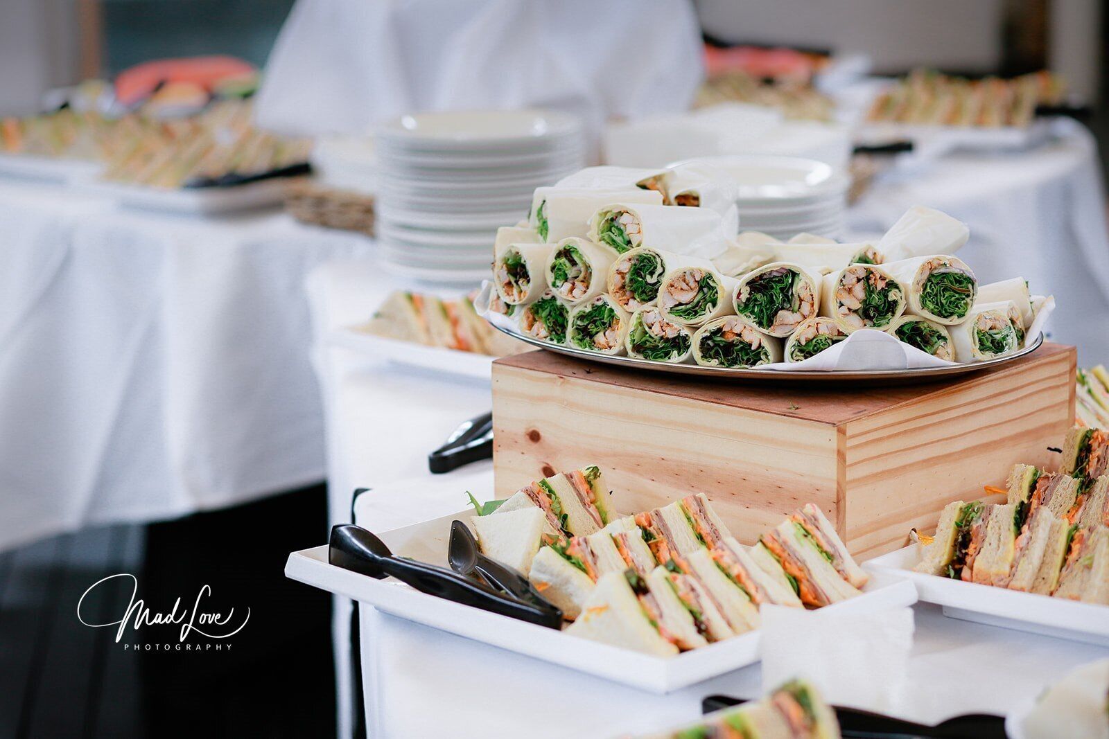 Een buffettafel met diverse belegde broodjes en rolletjes, waarvan sommige in papier verpakt en andere in driehoeken gesneden.