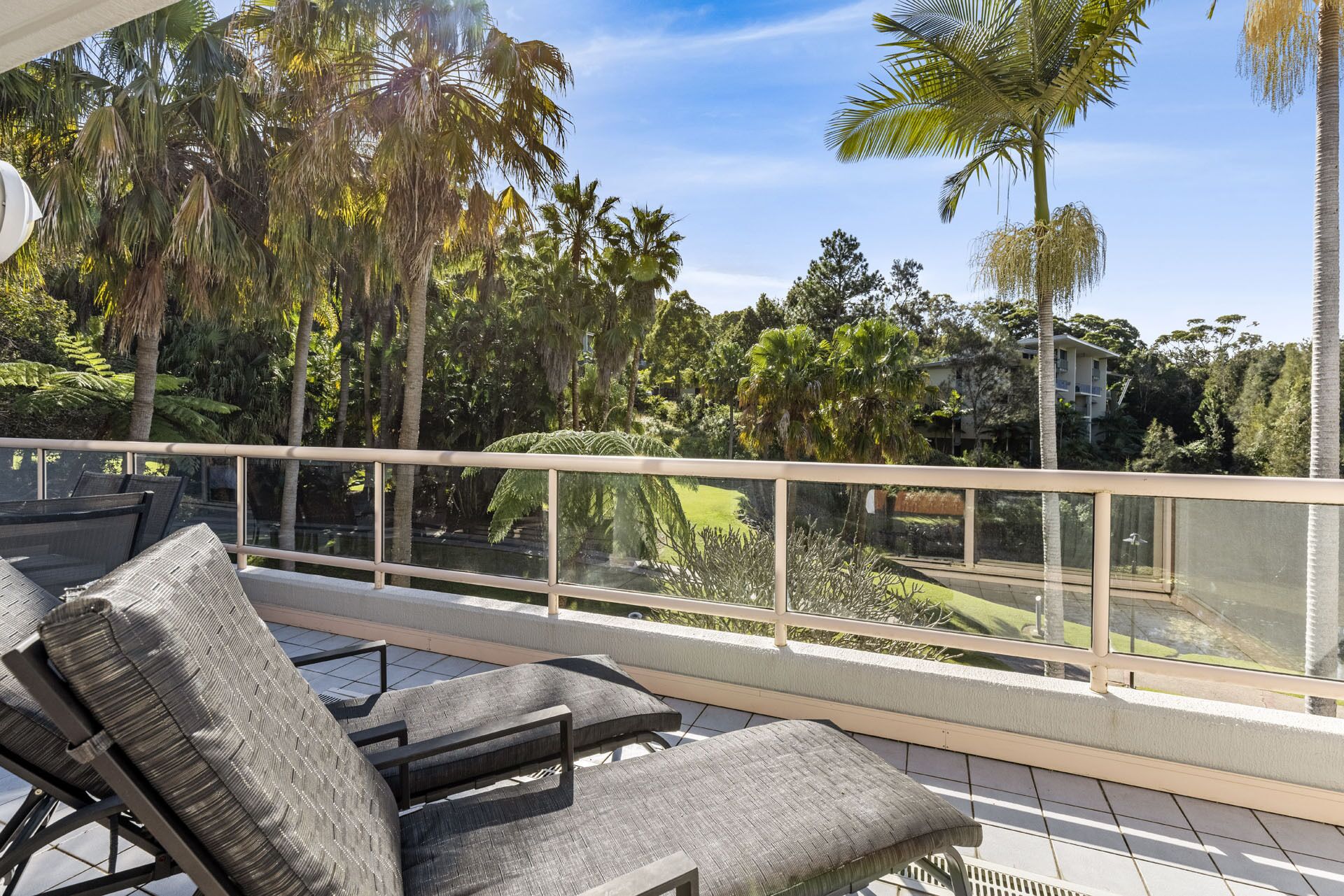 A balcony with outdoor seating, surrounded by lush greenery and palm trees.