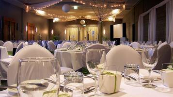 A banquet hall with round tables set for a formal event, complete with white tablecloths, glassware, and chairs.