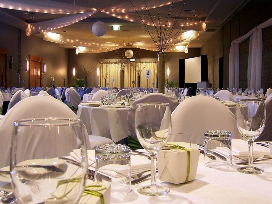 A banquet hall with round tables set for a formal event, complete with white tablecloths, glassware, and chairs.