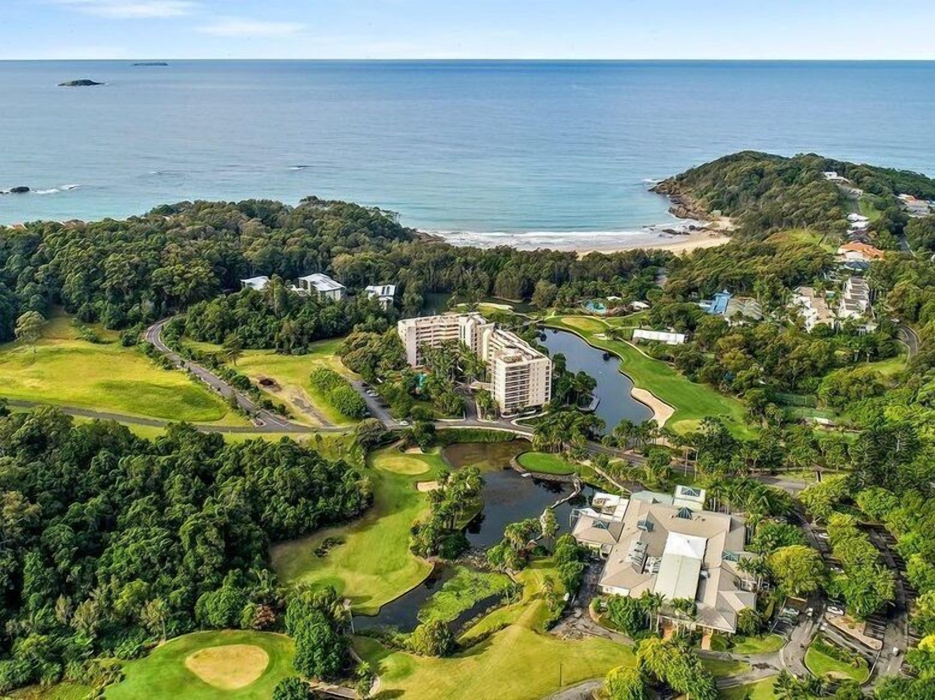 Vista aérea de un campo de golf con un edificio grande, una masa de agua y una playa.