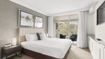 A modern bedroom with a large bed, a nightstand, a TV, and a balcony with outdoor seating.