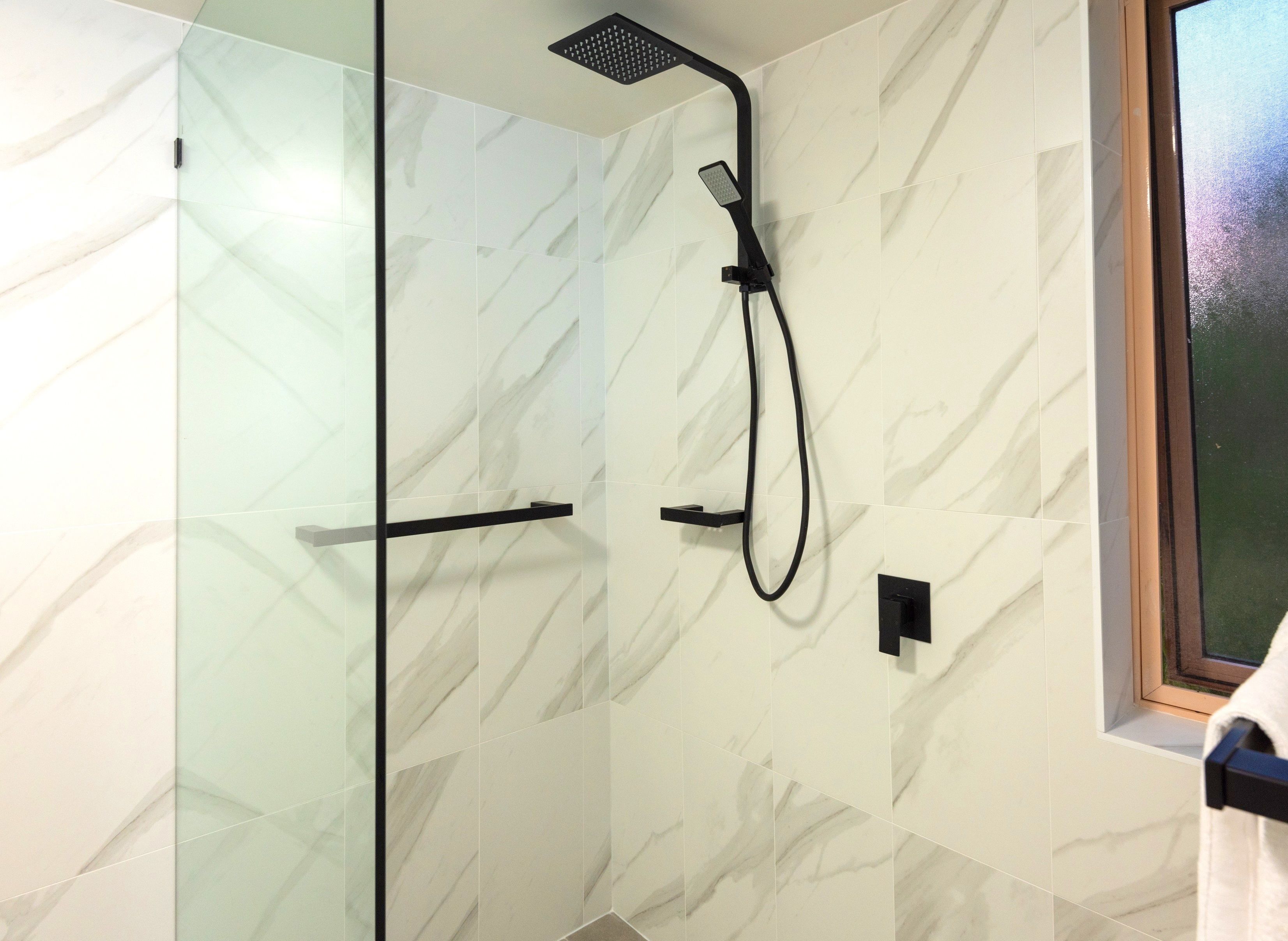 Een moderne douche met een glazen deur, een handdouche en een bedieningspaneel.
