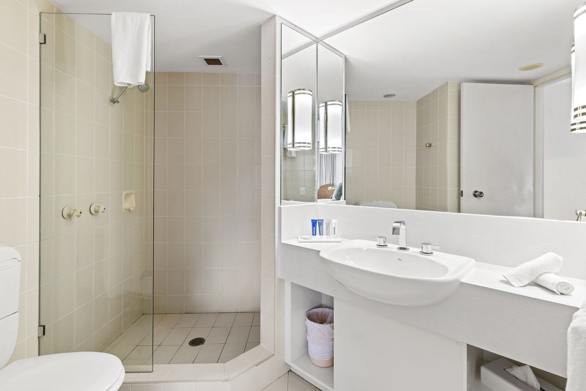 A modern bathroom with a glass-enclosed shower, a white sink, and a large mirror.