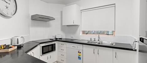 A modern kitchen with white cabinets, a black countertop, a built-in microwave, a kettle, and a window above the sink.