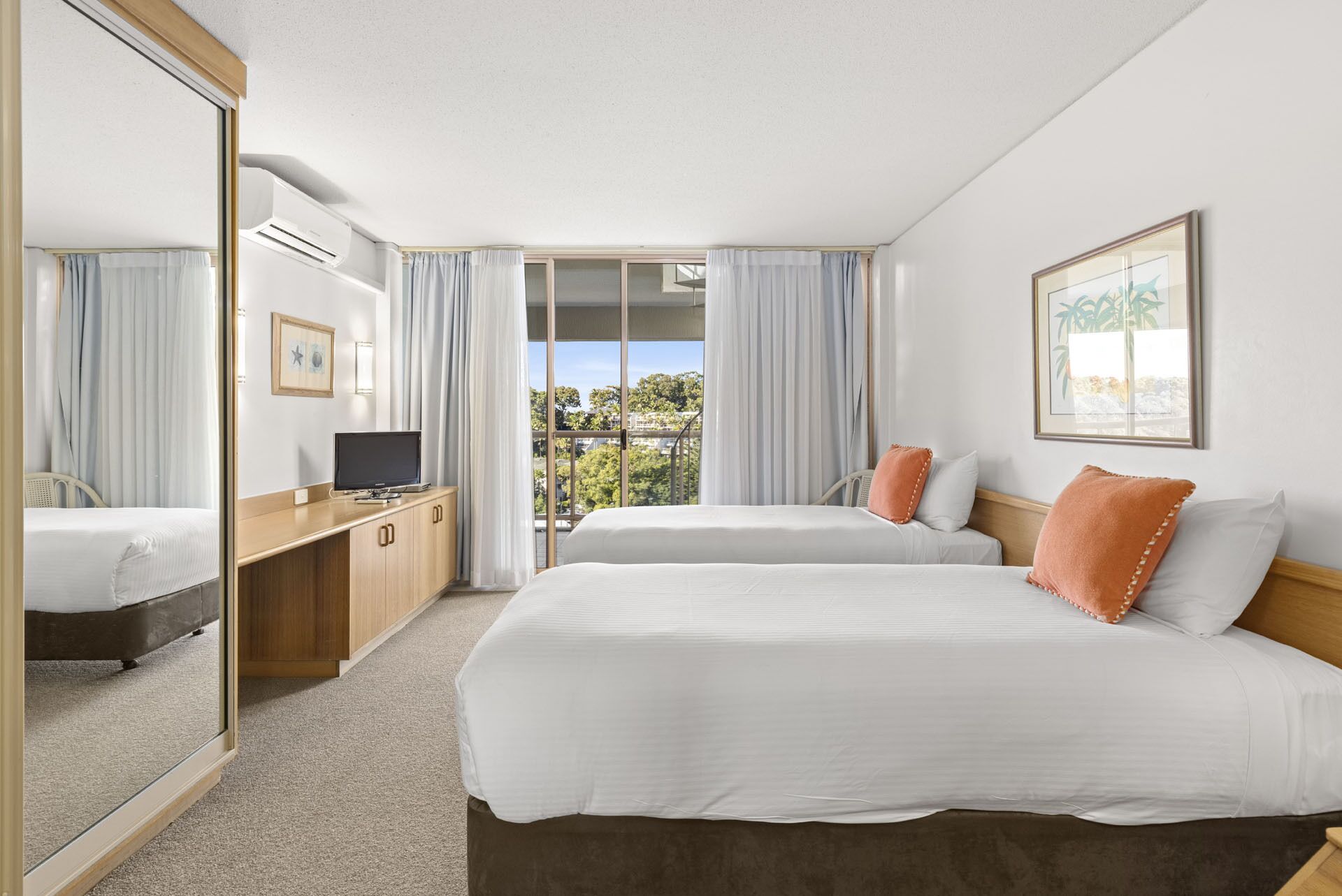Habitación de hotel con dos camas, televisión, escritorio y un amplio ventanal con cortinas.