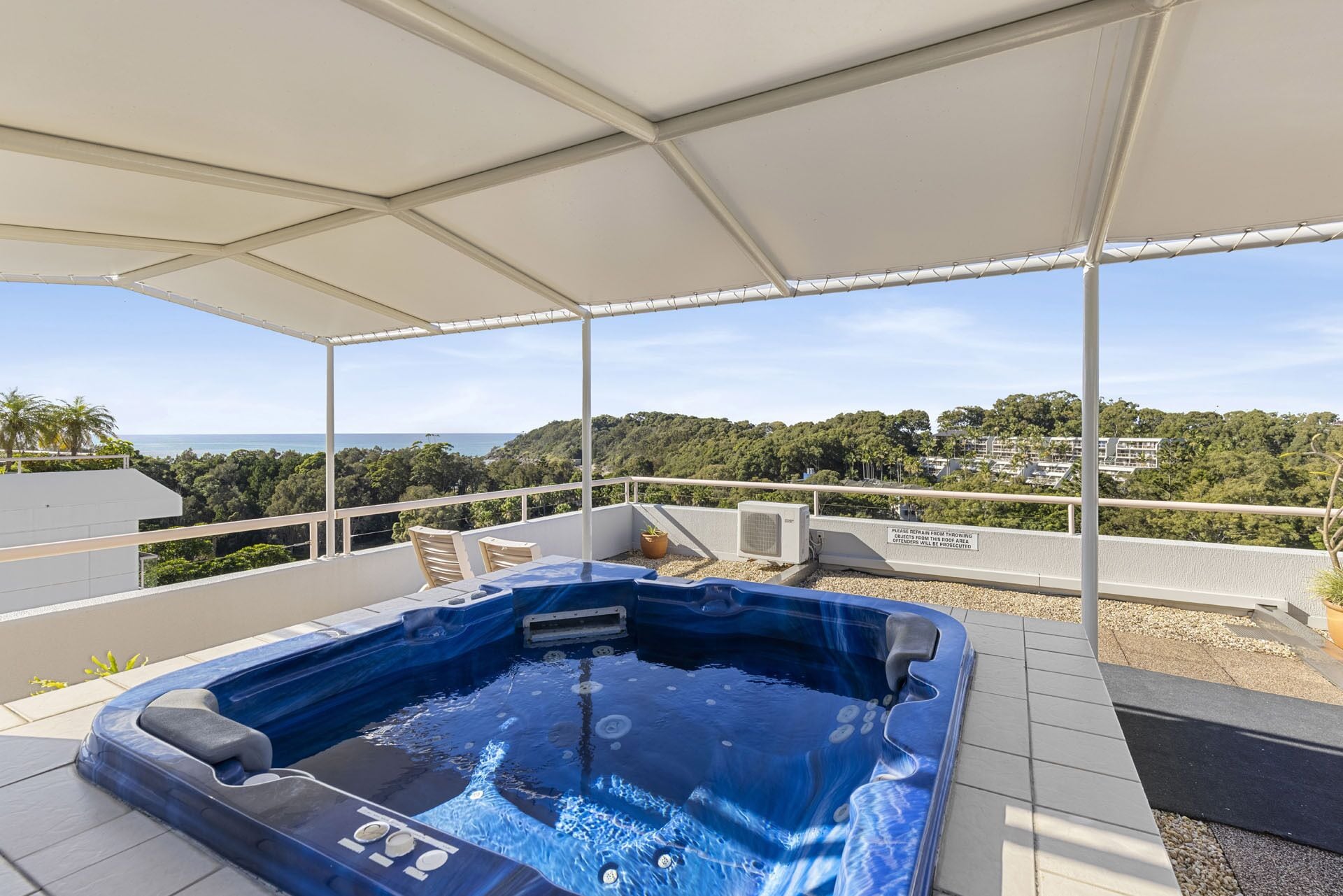 A hot tub under a covered patio with a view of the ocean and hills.