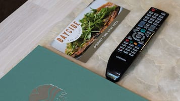 A teal-colored book with a logo, a remote control, and a menu card on a wooden surface.