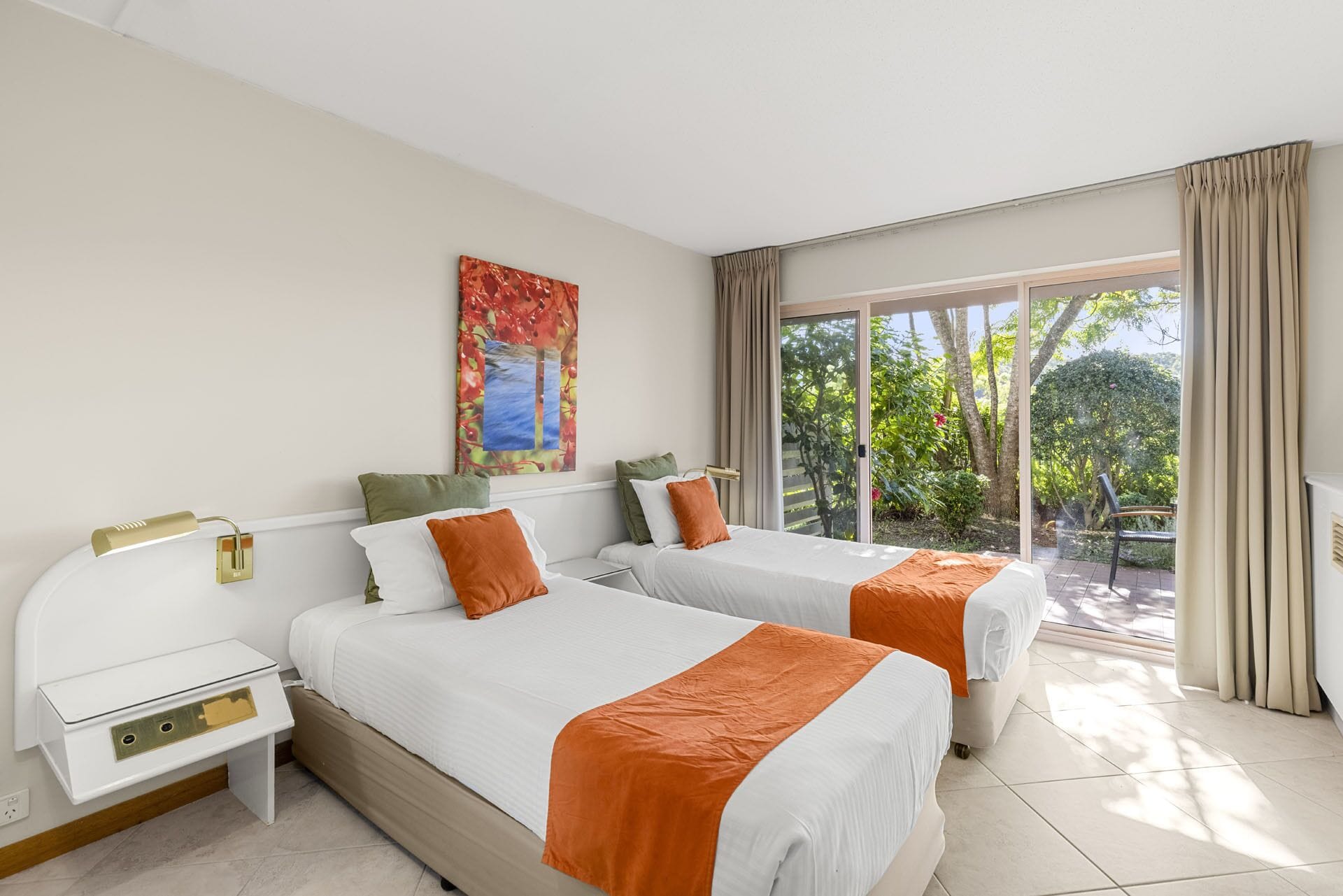 A hotel room with two beds, a nightstand, a desk, and a large window with a view of greenery.