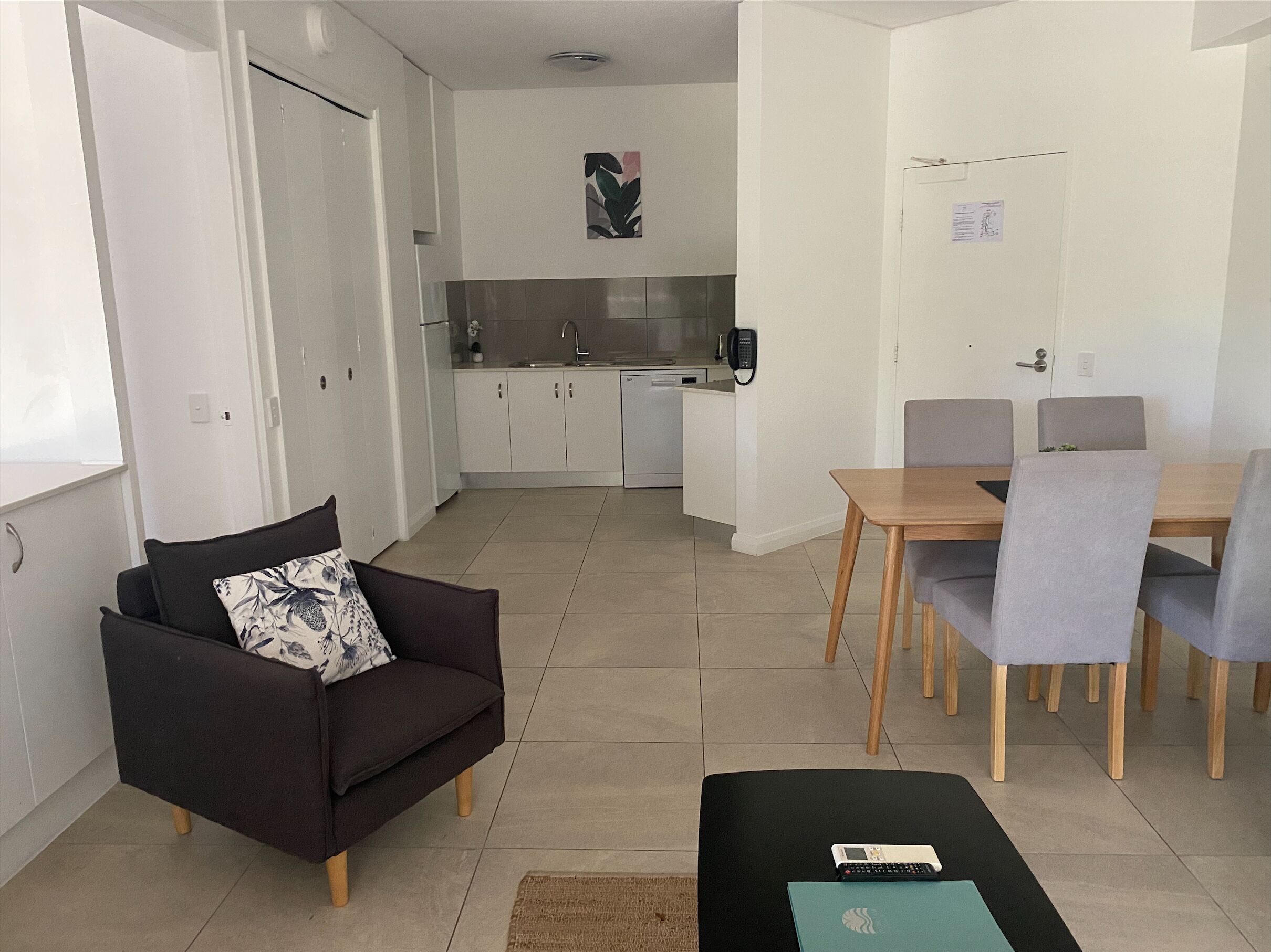 A modern living room with a sofa, a dining table with chairs, a kitchen area, and a small office space.