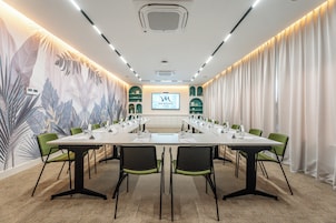 Un salón de conferencias con una larga mesa, sillas verdes, una pantalla y un mural.