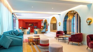 Un moderno vestíbulo de hotel con sofá, otomanas y sillones, un mostrador de recepción y una pared de acento roja.