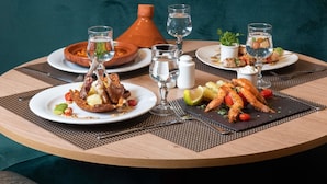 A round dining table with a variety of dishes, including seafood and meat, accompanied by glasses of water and wine. - Hotel Mercure Rabat Sheherazade (Rabat)
