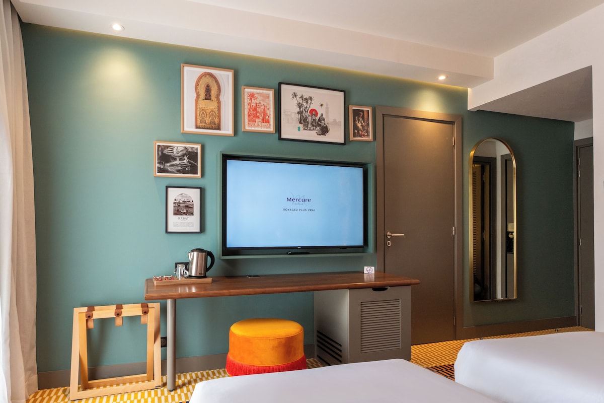 Habitación de hotel con televisión, cuadros en la pared, un escritorio de madera y una cama.