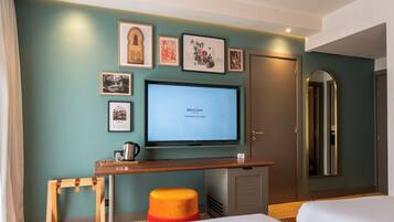 Habitación de hotel con televisión, cuadros en la pared, un escritorio de madera y una cama.