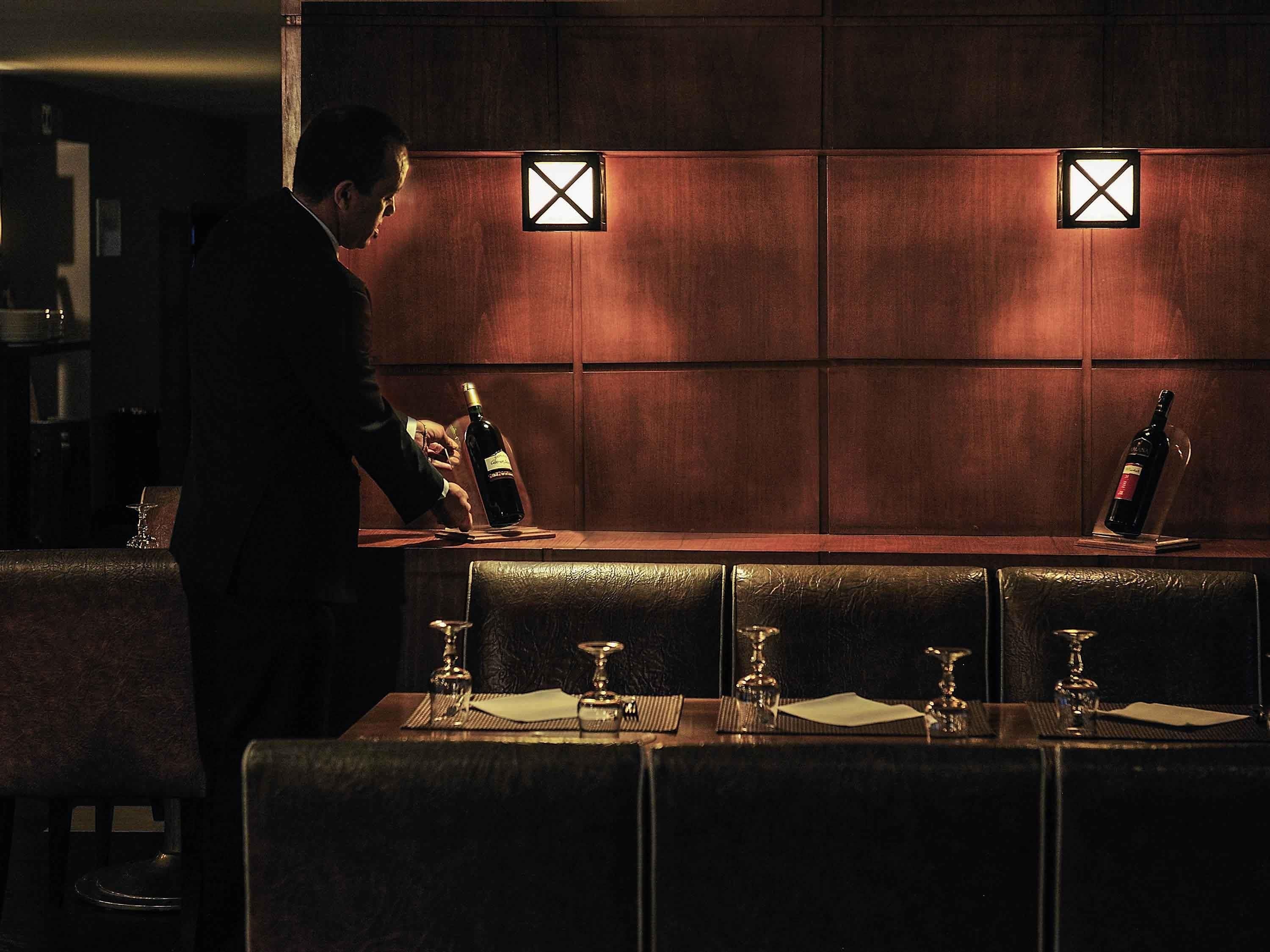 A bar area with a person pouring a drink, a bottle of wine, and glasses on the counter.