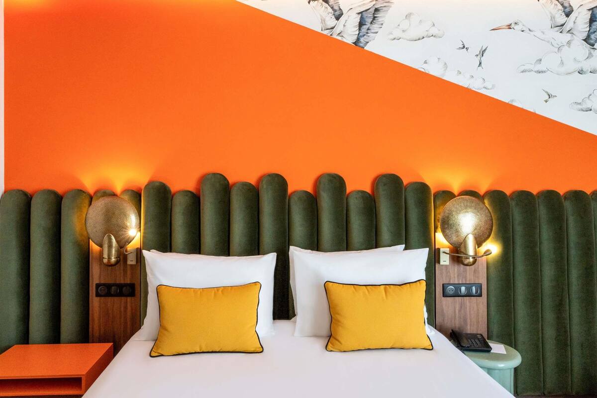 A hotel room with a large bed, two pillows, a nightstand, a telephone, and a wall with a mural.