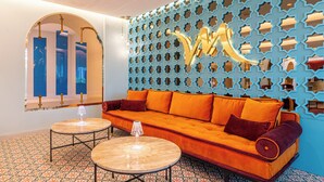 Un interior moderno con un sofá, dos mesas redondas, baldosas de suelo con diseño y una pared decorativa con formas geométricas.