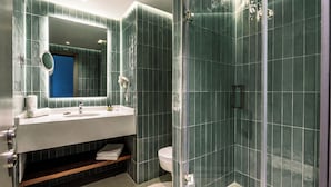 Un baño moderno con ducha de vidrio, un lavamanos blanco con espejo y una puerta azul.
