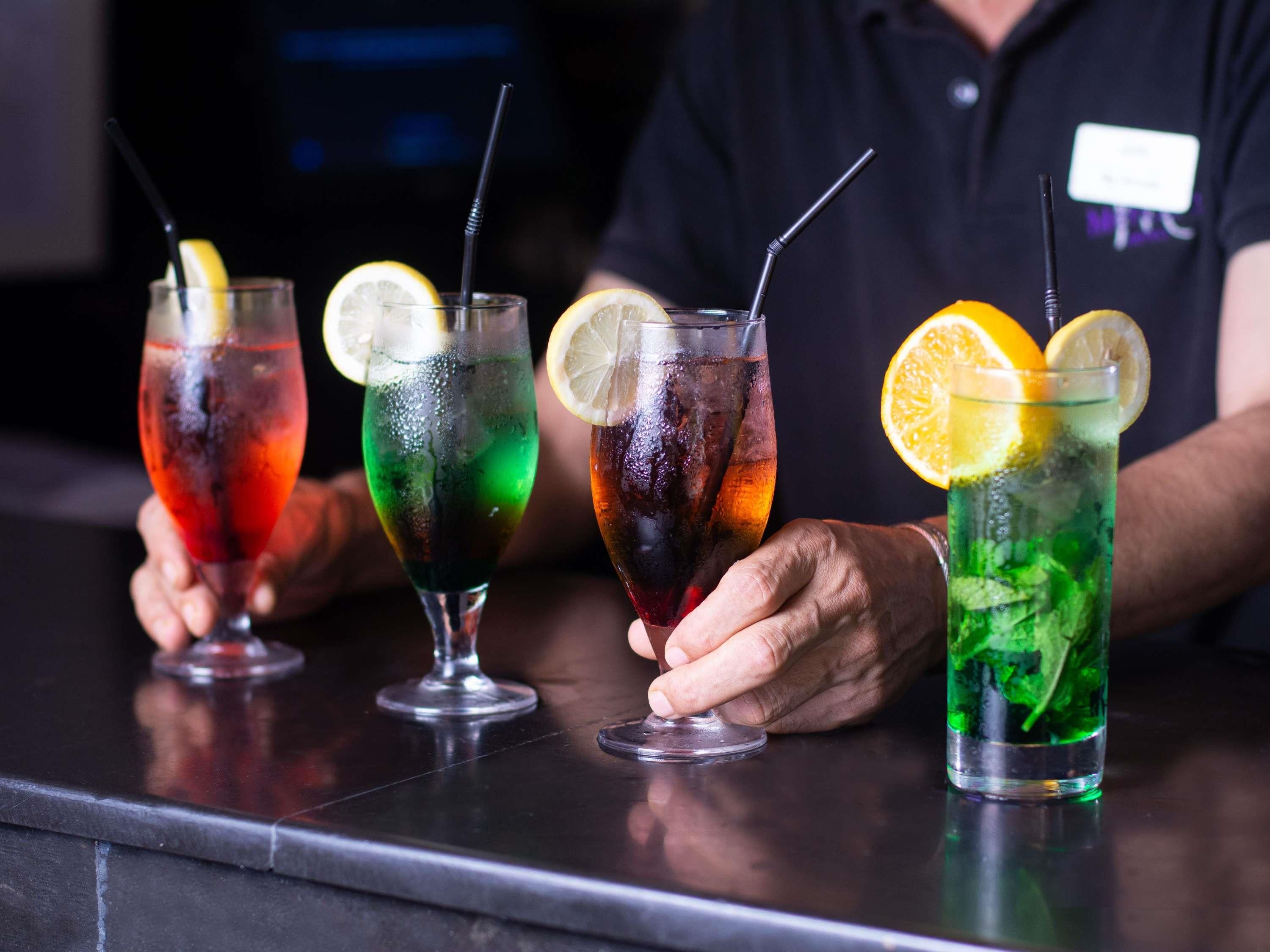 Four colorful cocktails with straws and lemon slices on a bar counter.