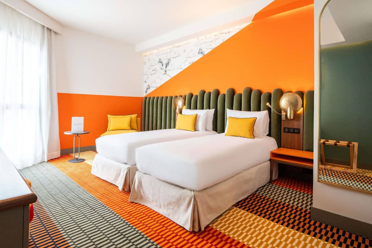 Quarto de hotel com duas camas, um espelho grande e um tapete estampado.