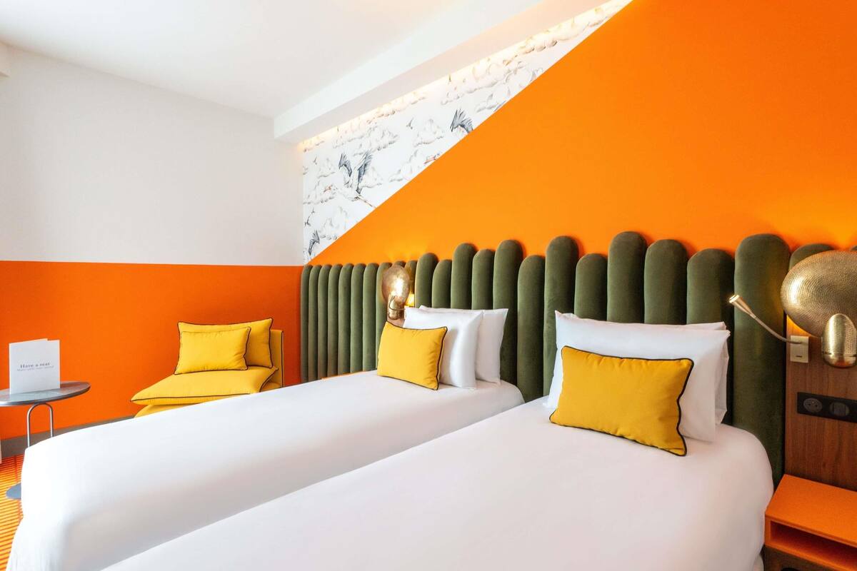 A hotel room with two beds, a small table, and a chair.