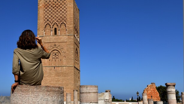 Una persona fotografiando una alta torre de ladrillo con diseños intrincados, ventanas en arco y motivos decorativos.