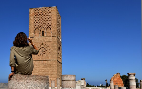 Una persona fotografiando una alta torre de ladrillo con diseños intrincados, ventanas en arco y motivos decorativos.