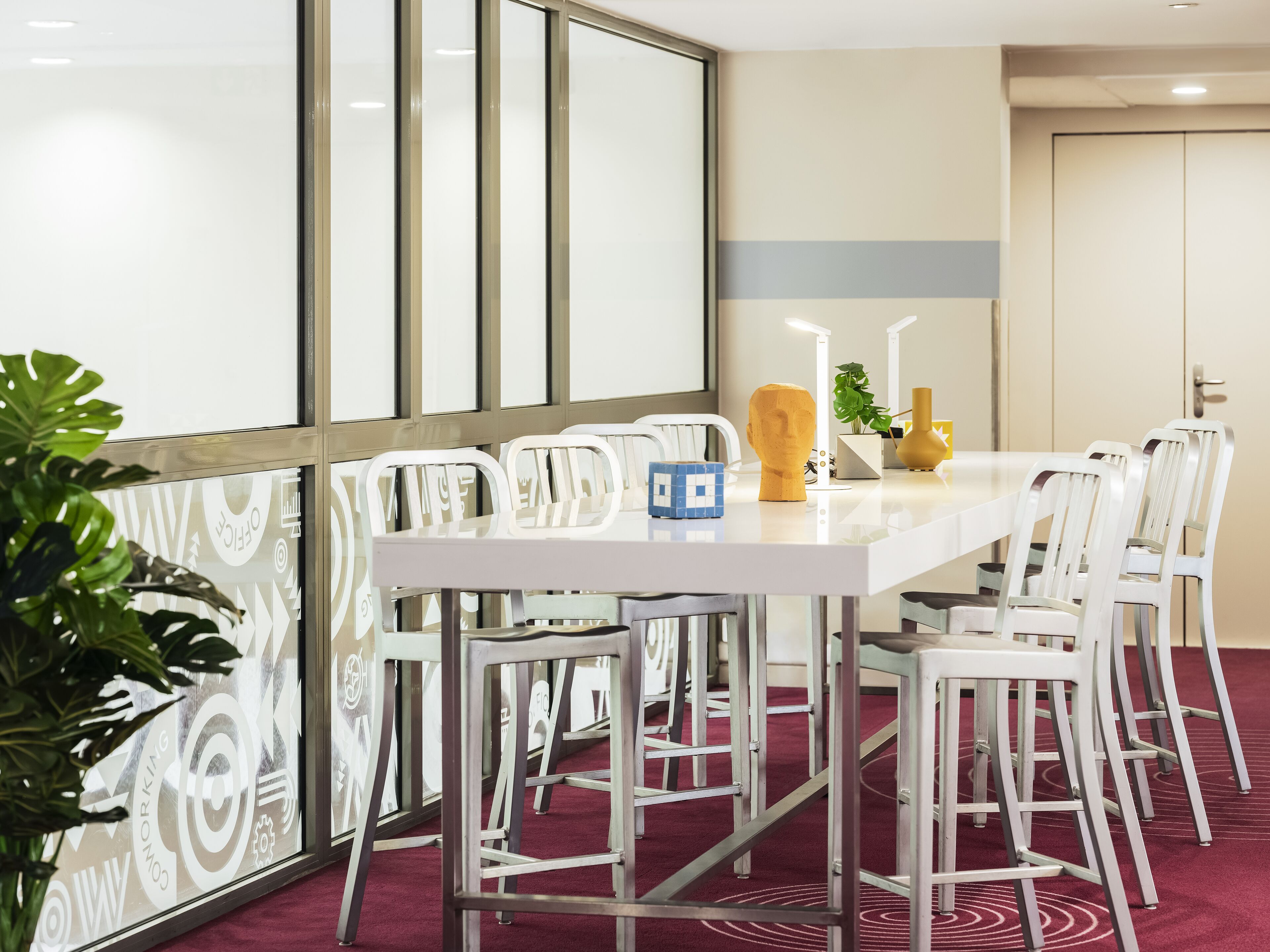 A conference room with a white table, white chairs, a potted plant, and a decorative vase.