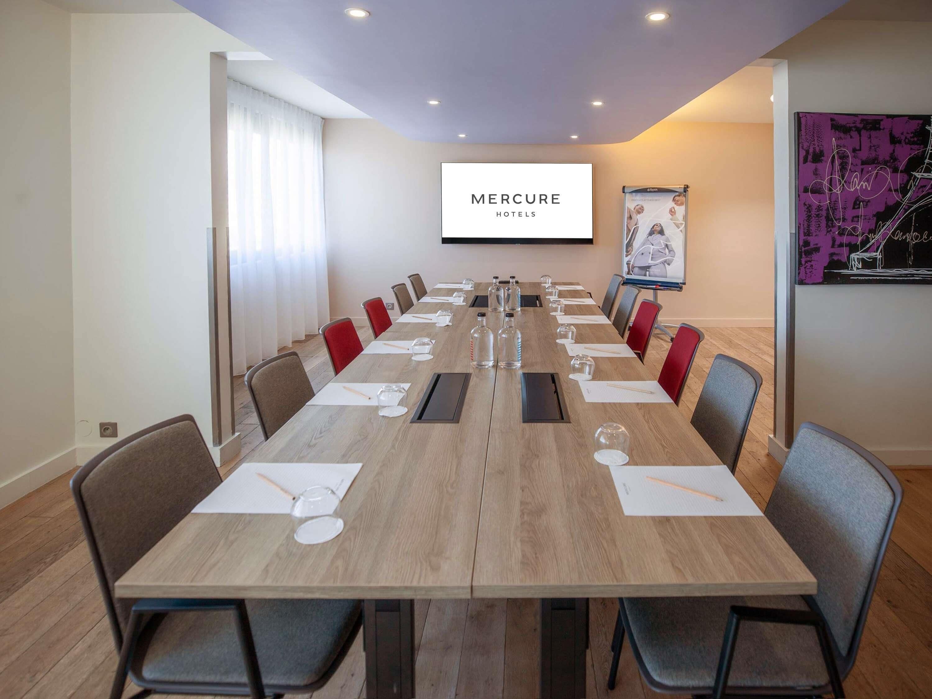 Un salón de conferencias con una larga mesa, sillas, una pantalla de proyector y una pizarra para presentaciones.