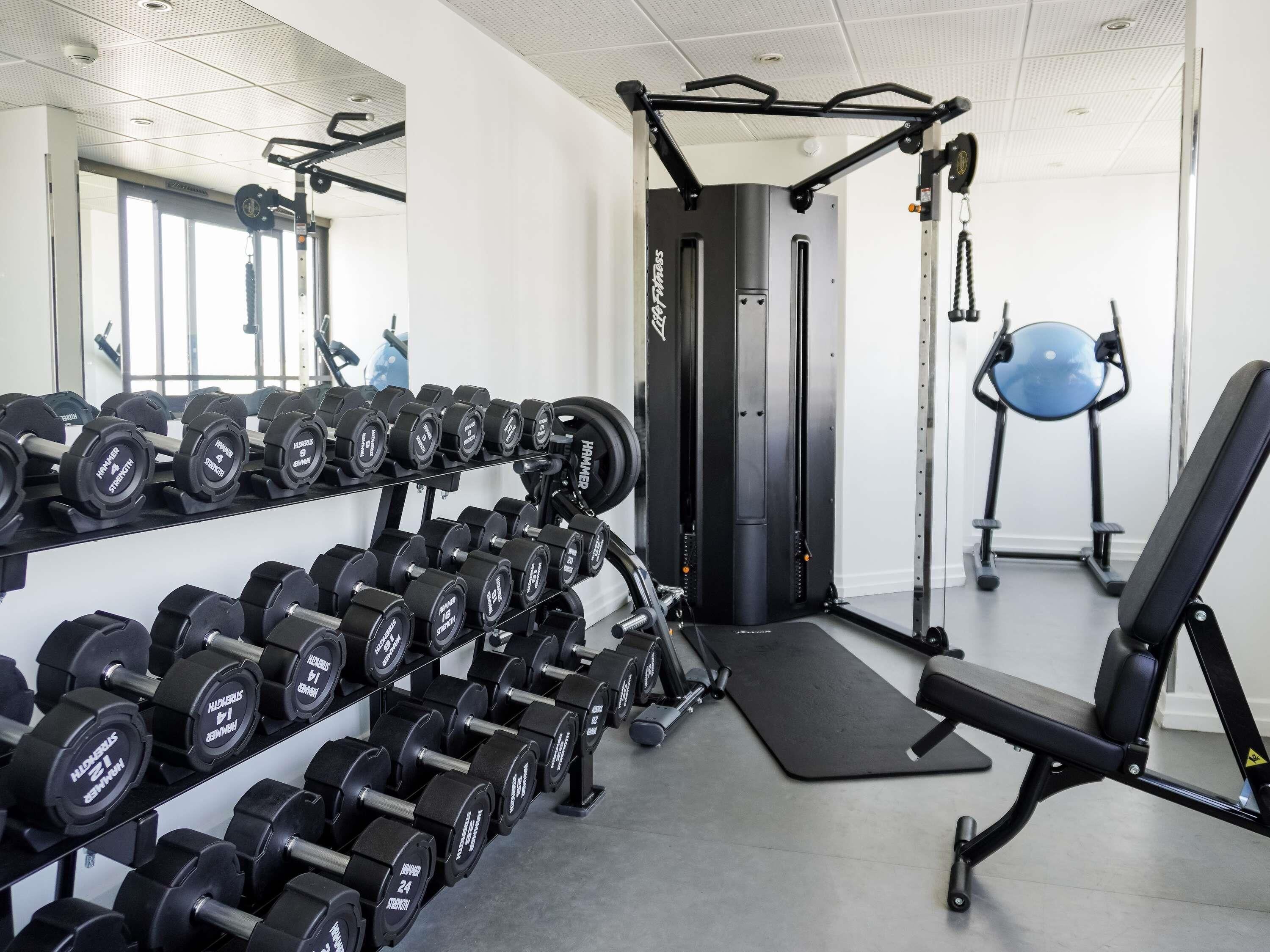 Uma academia com suportes para pesos, equipamentos de exercícios e um espelho grande.