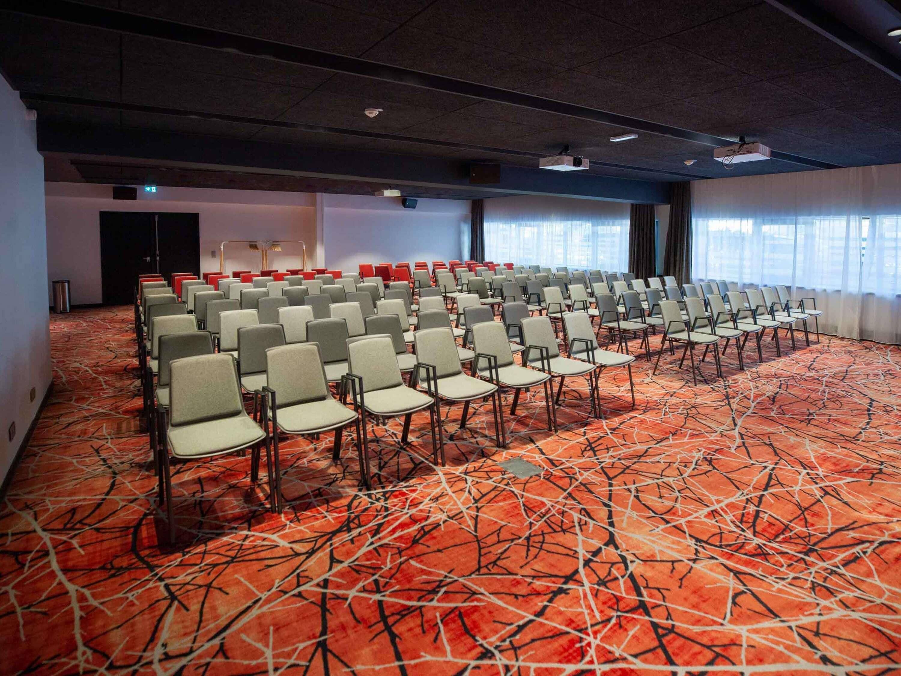 A conference room with rows of chairs, a carpeted floor, and a projector on the ceiling.