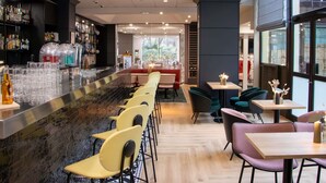 A modern bar area with a long counter, multiple seating options including bar stools and tables, and a view of the outdoors through large windows. - Mercure Paris Centre Tour Eiffel (Paris)