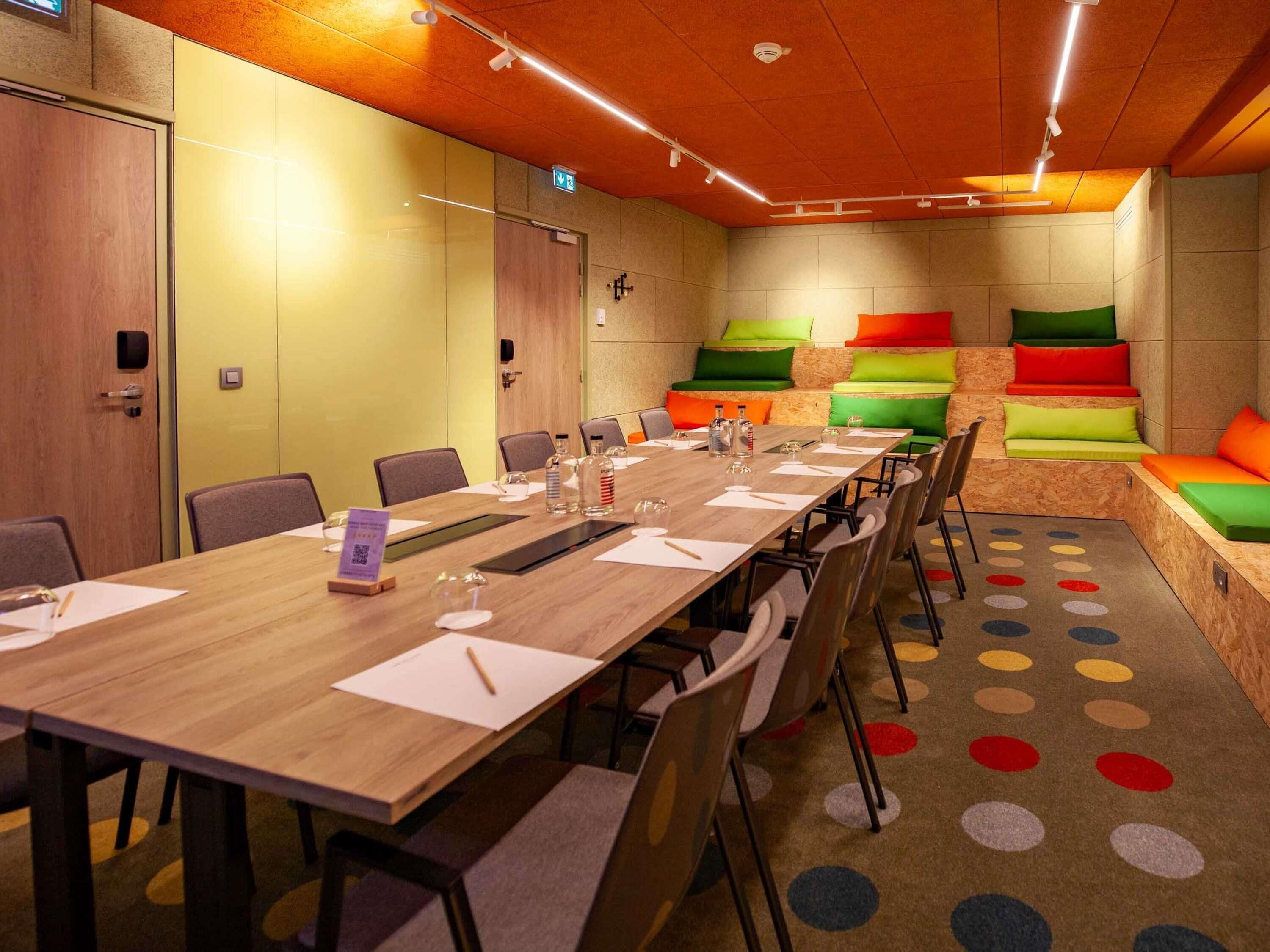 A conference room with a long table, chairs, a projector, and a colorful seating area.