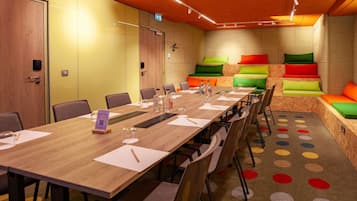 A conference room with a long table, chairs, a projector, and a colorful seating area.