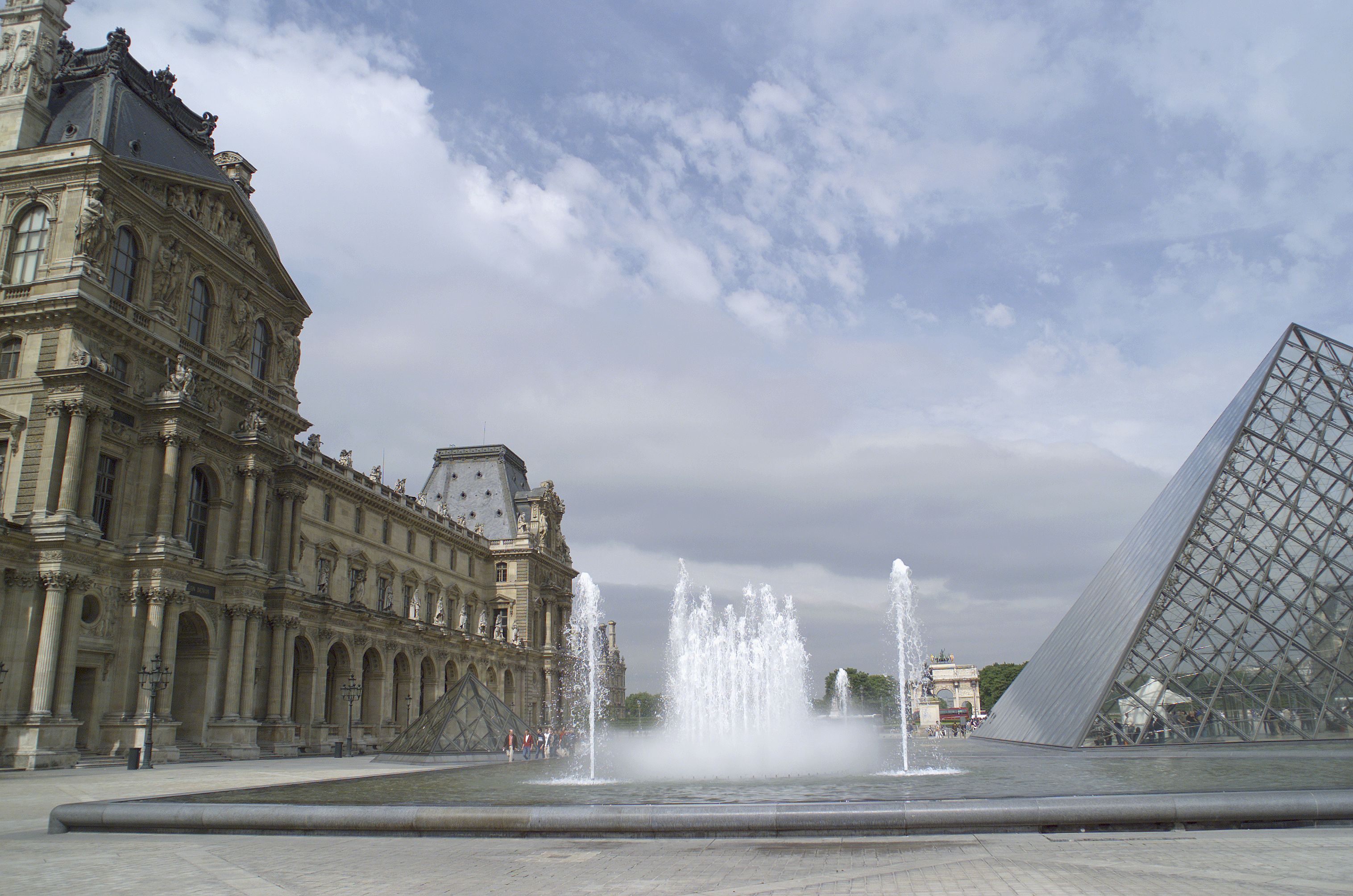 A grand historical building with a large fountain and a modern glass pyramid.