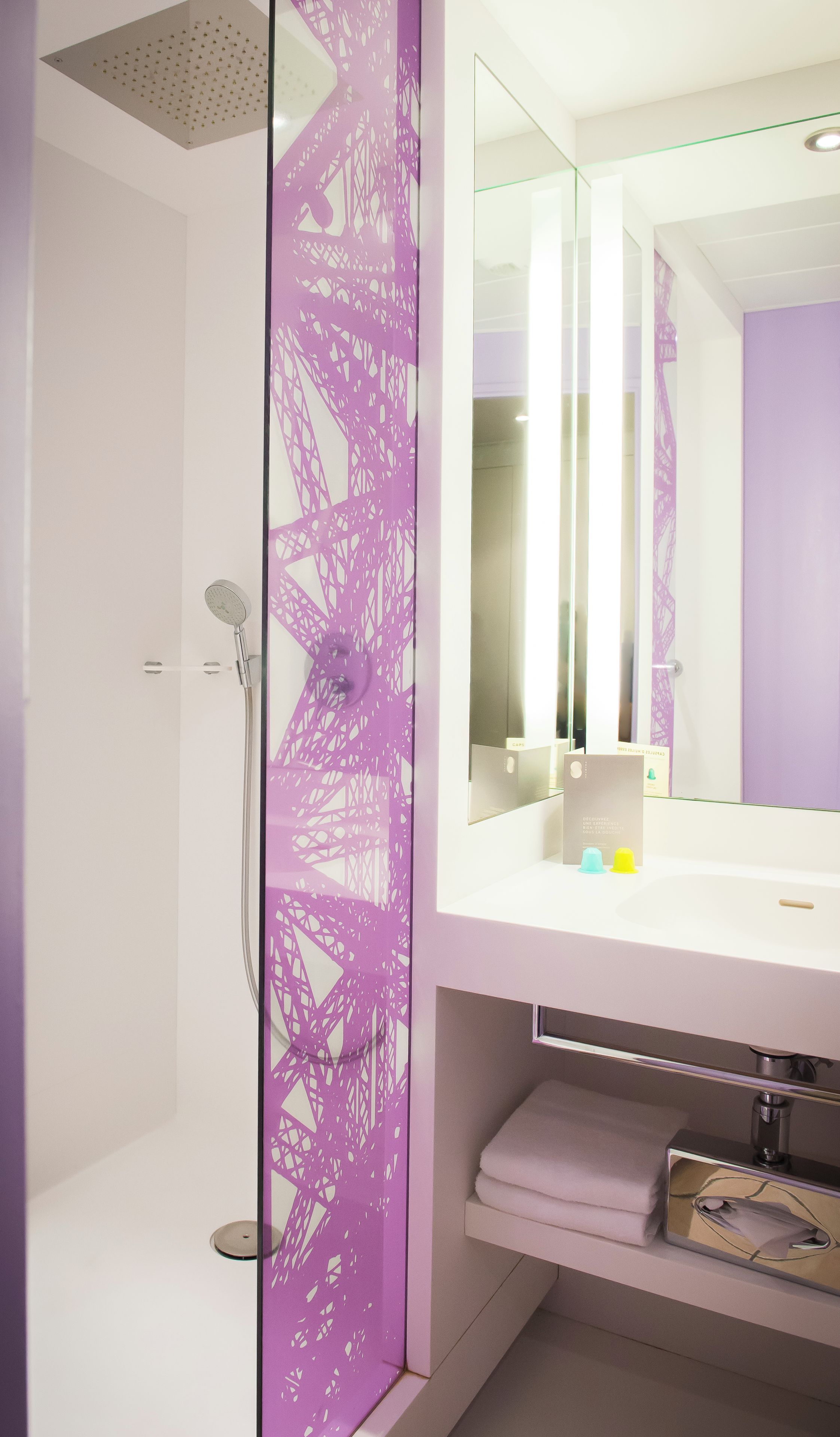 A modern bathroom with a shower, a large mirror, and a purple decorative panel.