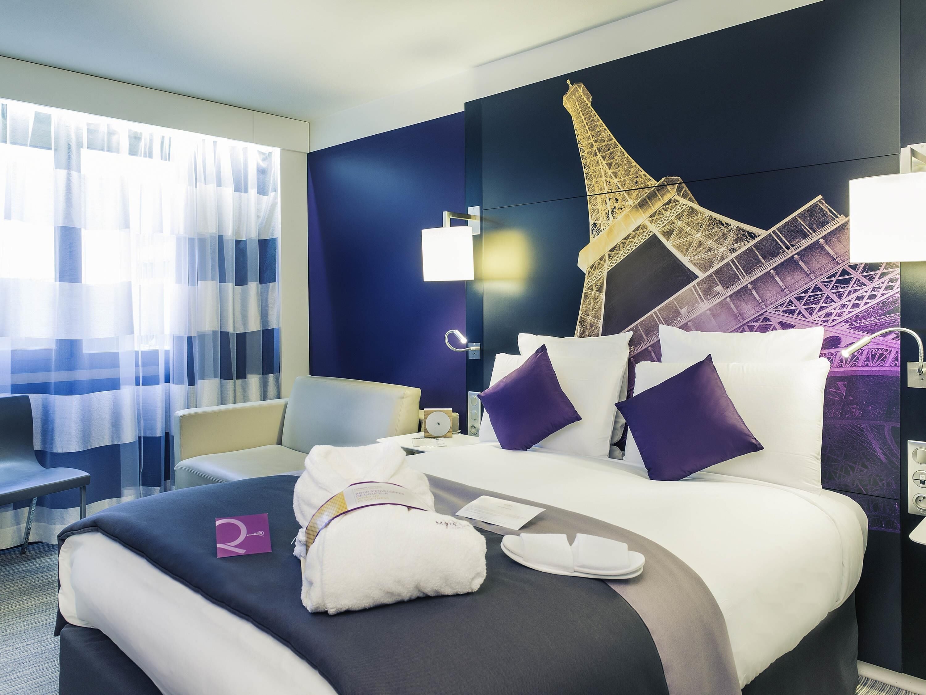 Habitación de hotel con cama, una silla, un escritorio y un gran mural en la pared de la Torre Eiffel.