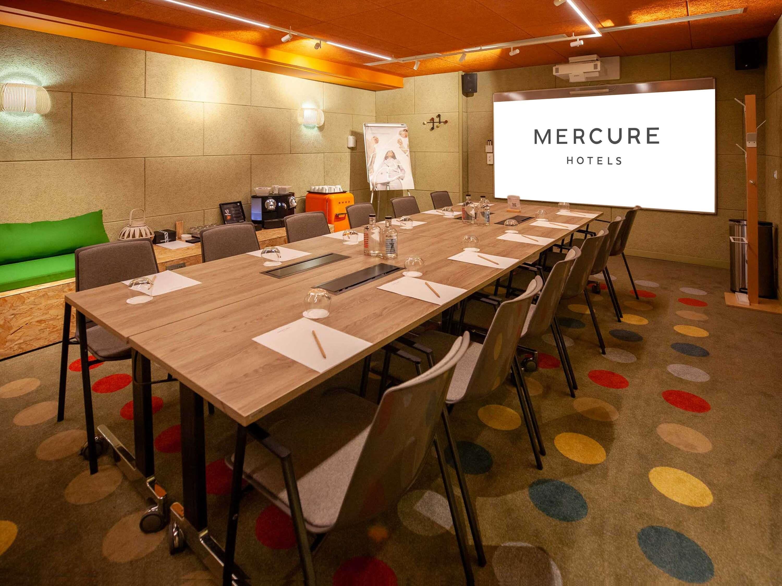 Un salón de conferencias con una mesa larga, sillas, una pantalla de proyector y un sofá verde.
