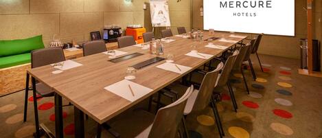 Un salón de conferencias con una mesa larga, sillas, una pantalla de proyector y un sofá verde.