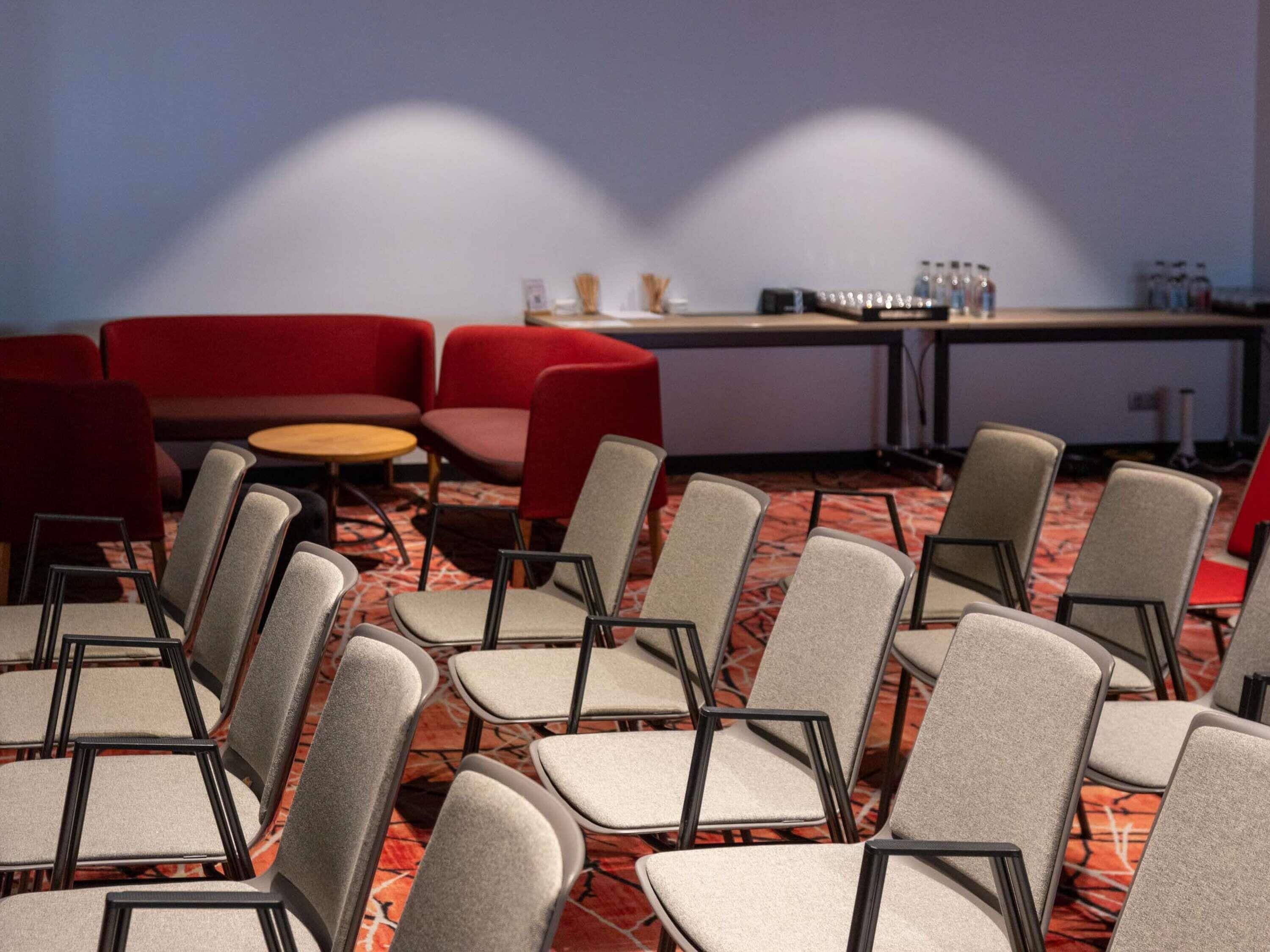 A conference room with rows of grey chairs, a red sofa, and a table with water bottles.