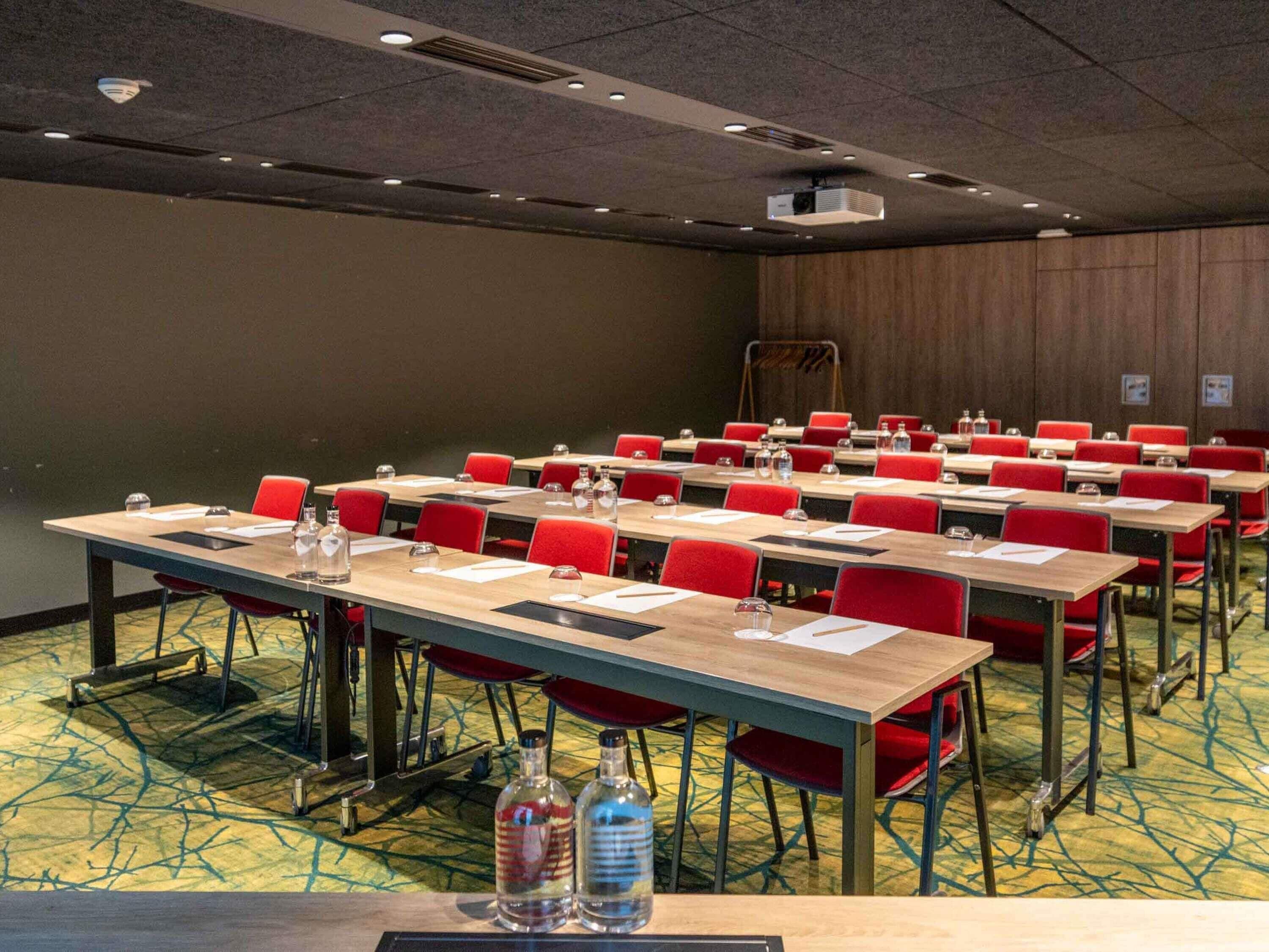 Une salle de conférence dotée de plusieurs tables et de chaises rouges, et équipée de bouteilles d’eau et de plaques nominatives.