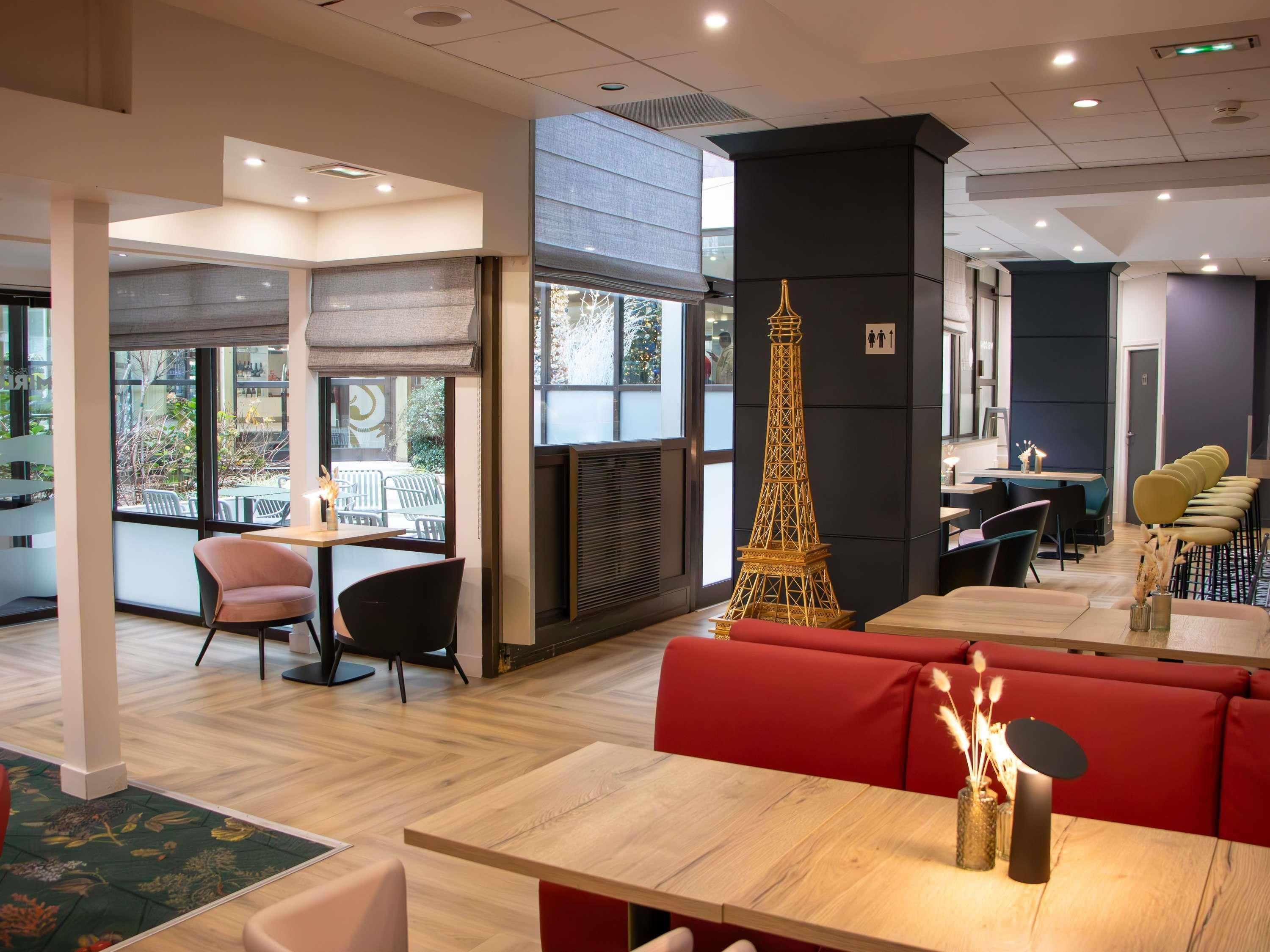 A modern interior with a dining area, a red sofa, a tall decorative structure resembling the Eiffel Tower, and a view through large windows.