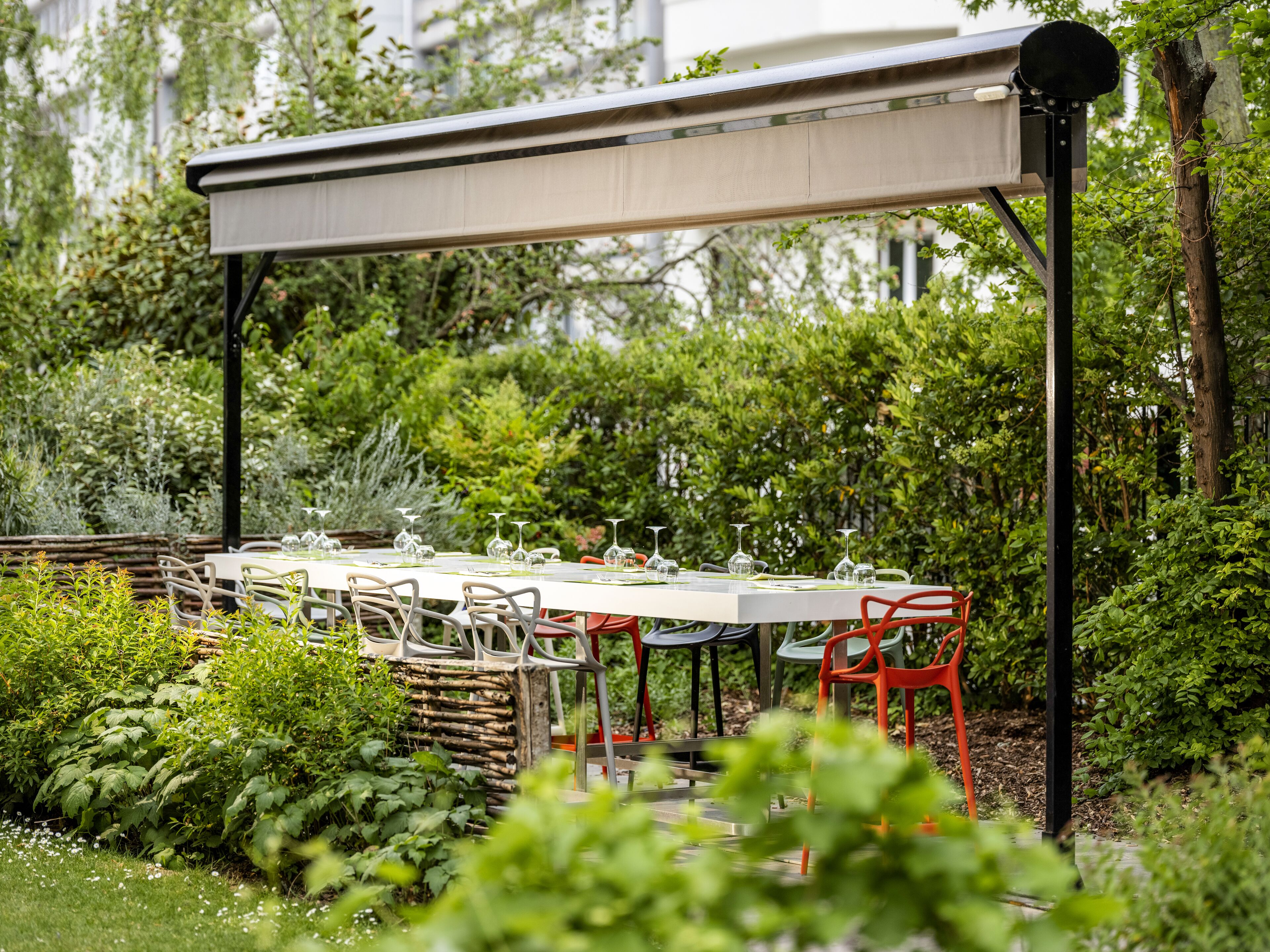 Un área de comedor al aire libre con una mesa y sillas cubiertas, rodeada de abundante vegetación.