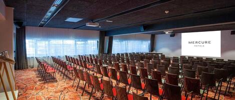 A conference room with rows of chairs, a projector screen, and a carpeted floor.