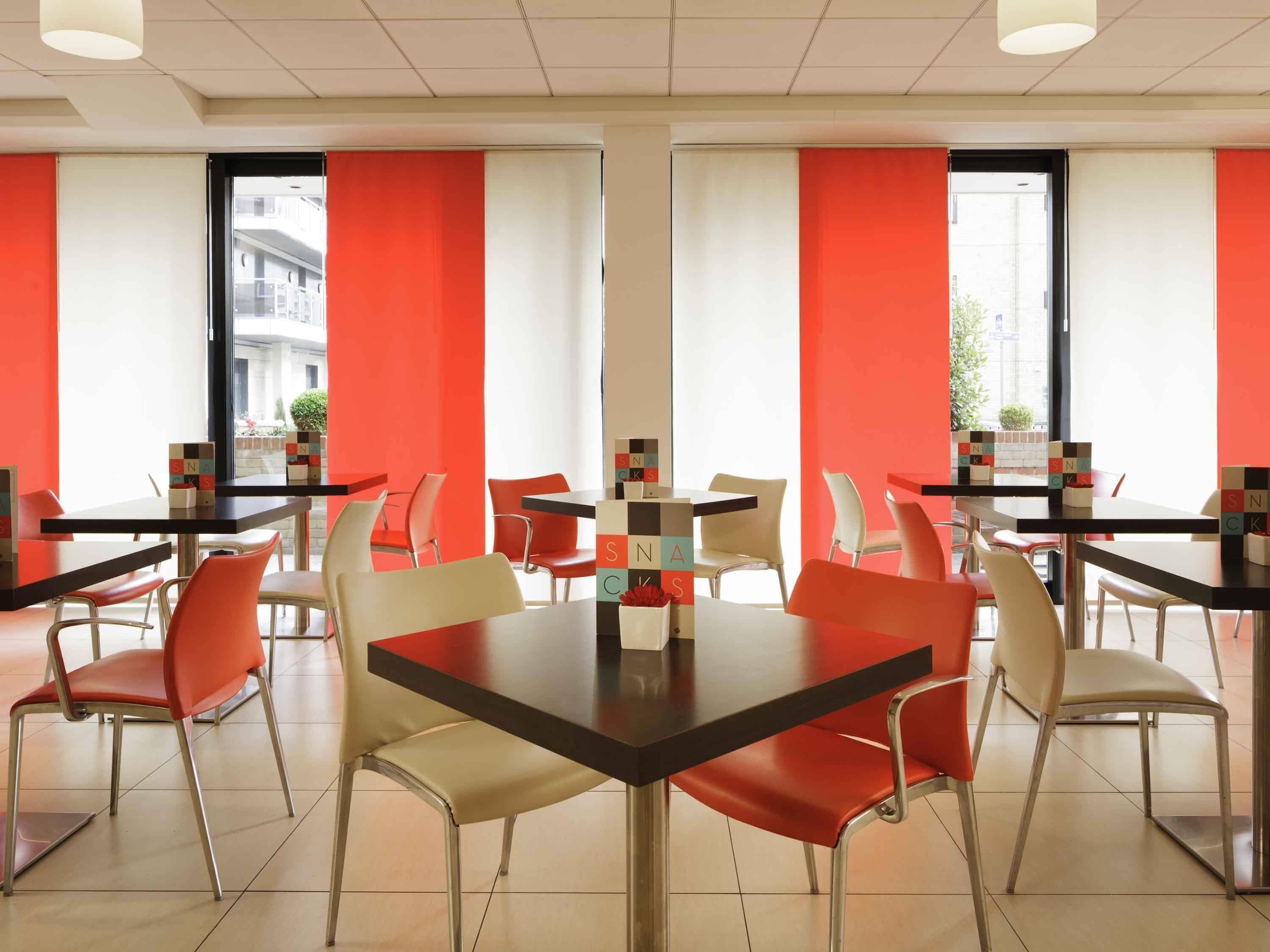 A modern dining area with tables and chairs, large windows, and a view of buildings outside.
